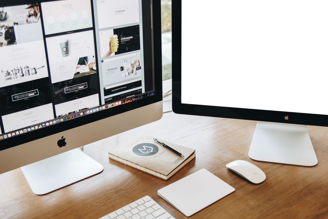 Vista dall'alto di una scrivania elegante con due monitor, tastiera, mouse e accessori contemporanei.